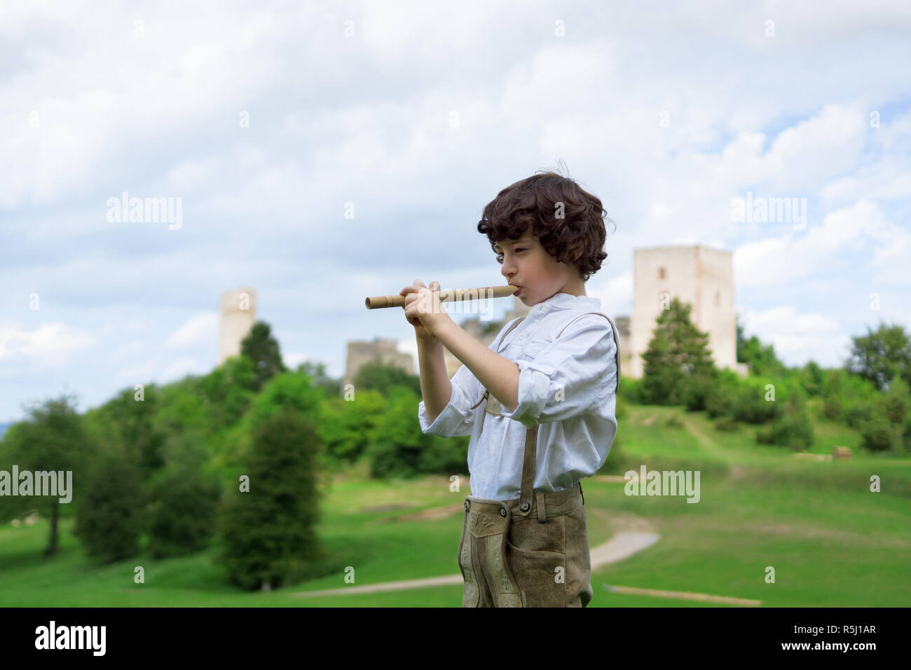 A boy in traditional Bavarian clothes with a shepherd's pipe on the background of ancient ruins. Stock Photo