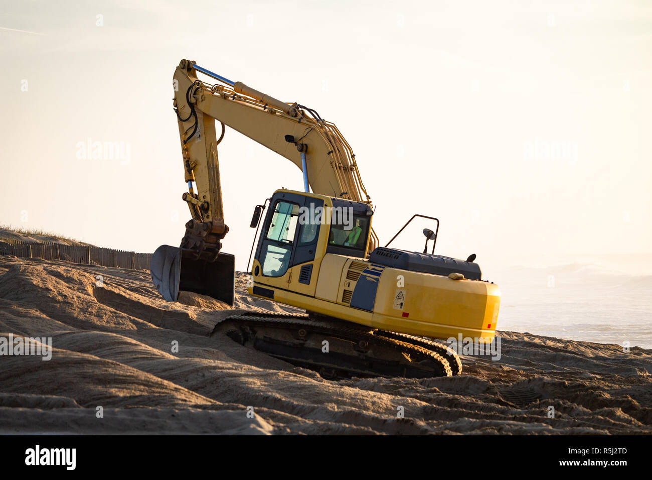 Yellow excavator gathers some sand at the beach. Warm light background. Copy space. Stock Photo
