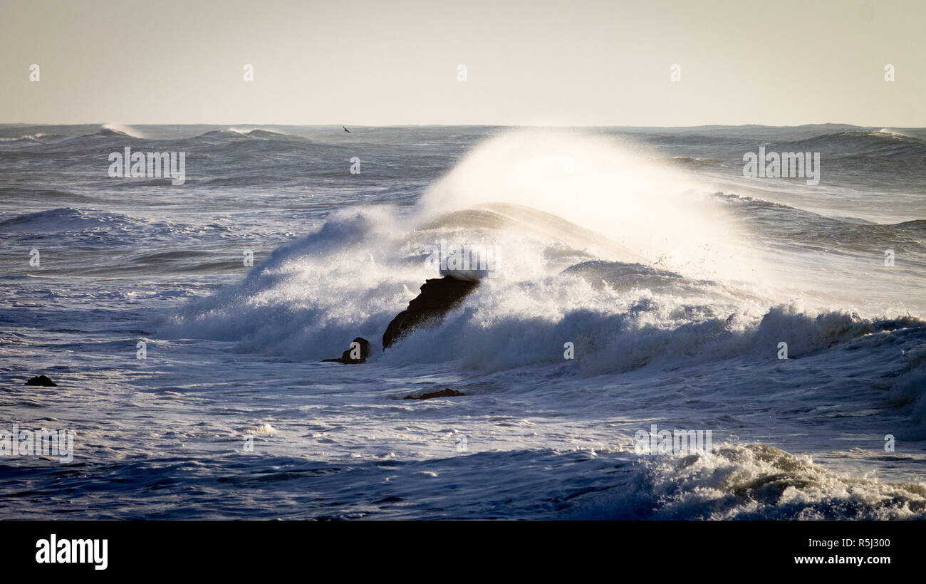 Waves crash on a rock in the sea, forming a circular moving shape in the water. Distant horizon line. Stock Photo