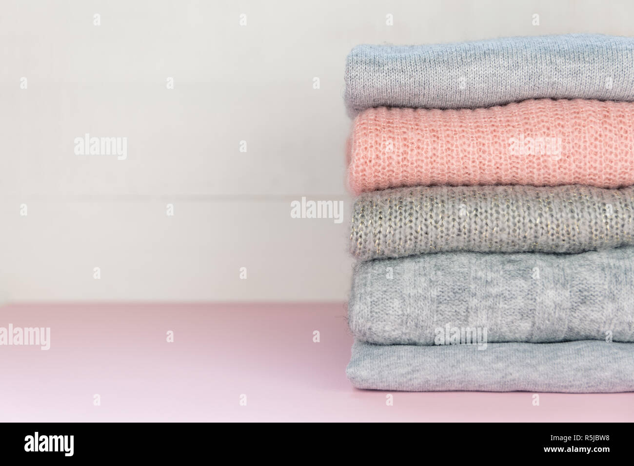 Four grey and one pink folded knitted jumpers laying on pastel pink surface. Stock Photo