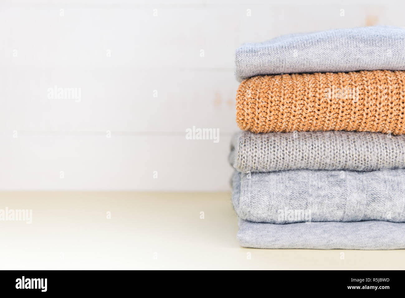 Four grey and one yellow folded knitted jumpers laying on yellow pastel surface. Stock Photo