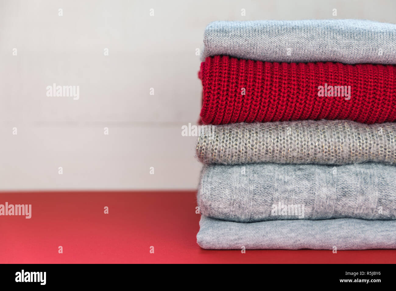 Four grey and one red folded knitted jumpers laying on red surface. Stock Photo