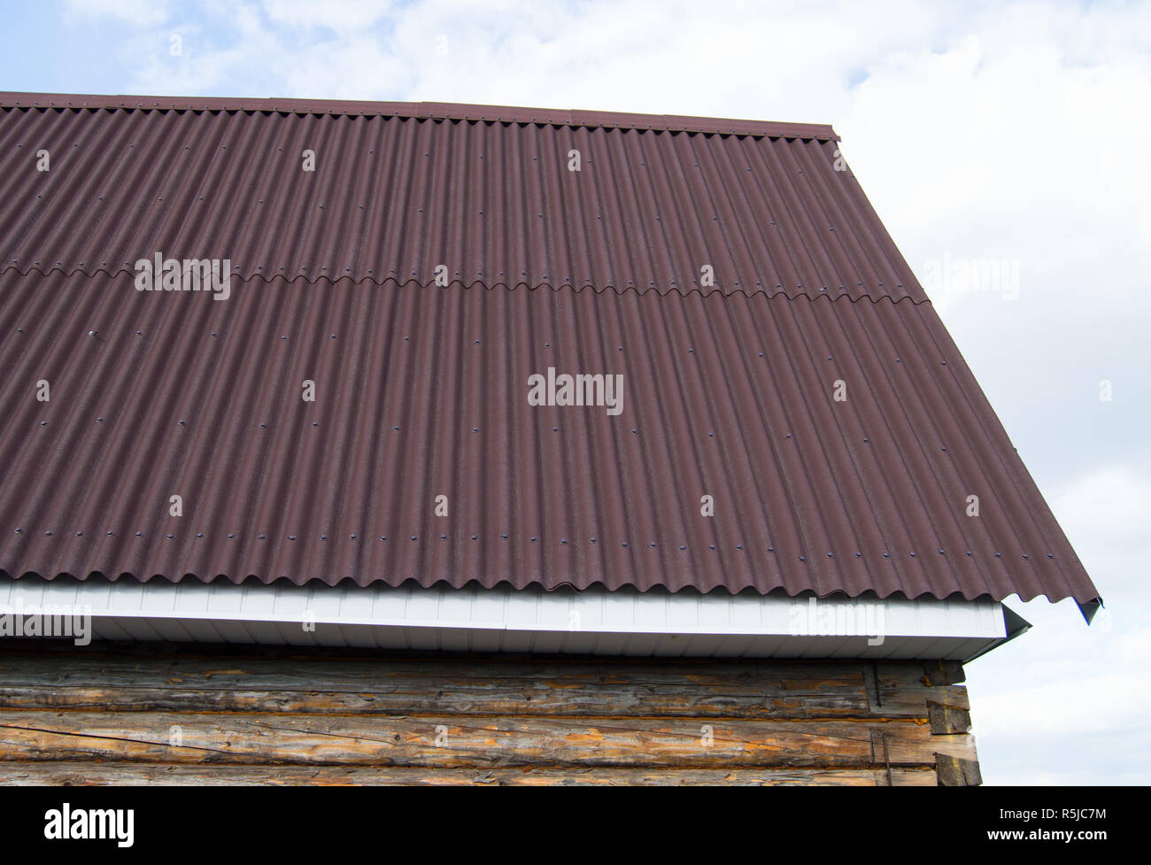 modern construction of the roof with red metal siding to a wooden house in the garden Stock Photo