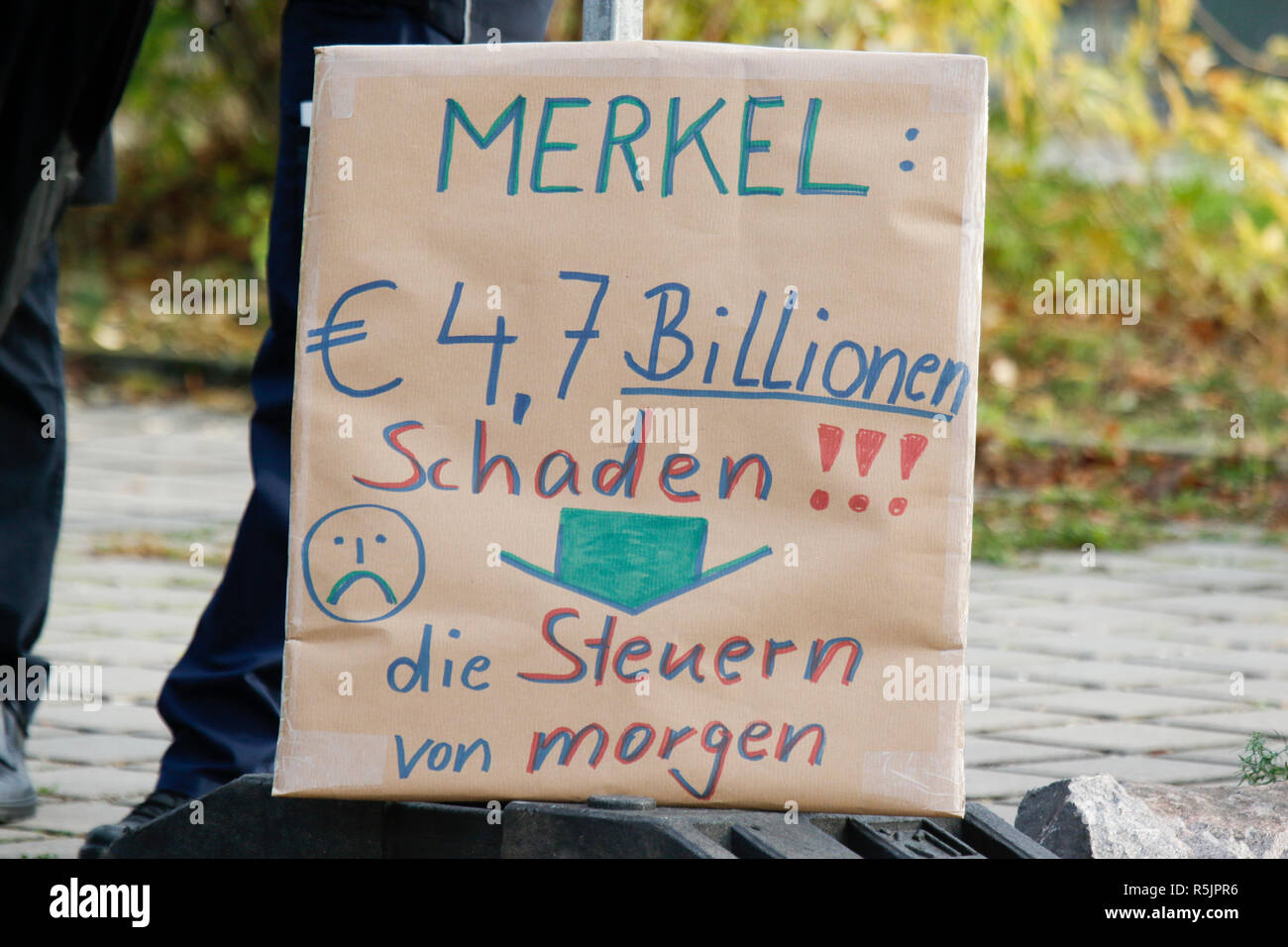 Kandel, Germany. 1st December 2018. A protester holds a sign that reads 'Merkel: 4,7 Billion damage!!! The taxes of tomorrow'. Around 250 people from right-wing organisations protested in the city of Kandel in Palatinate against the German government. They also adopted the yellow vests from the French yellow vest protest movement. The place of the protest was chosen because of the 2017 Kandel stabbing attack, in which a 15 year old girl was killed by an asylum seeker. They were confronted by anti-fascist counter-protesters from different political parties and organisations. Credit: Michael Deb Stock Photo