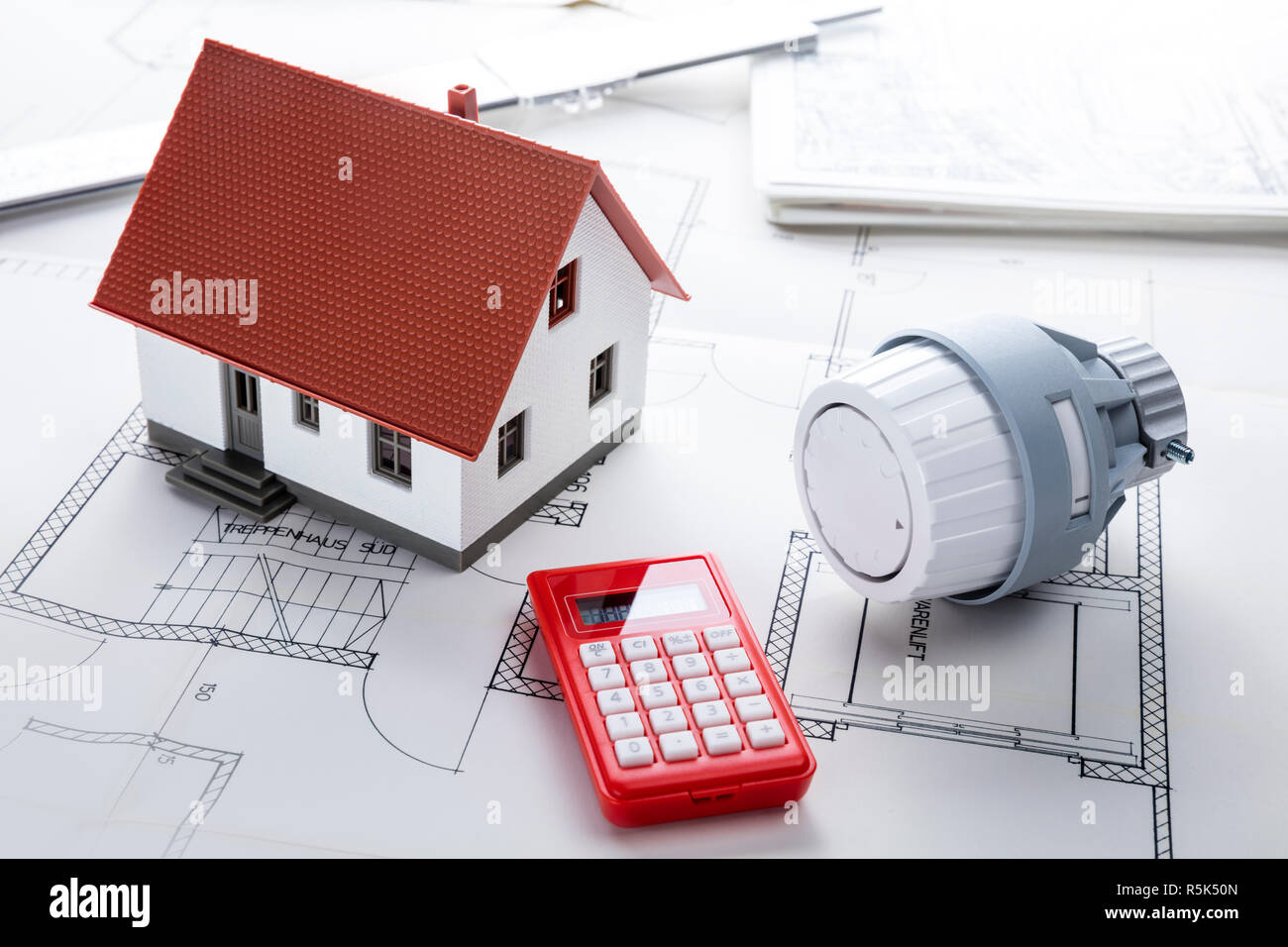 on a blueprint plan stand a house a thermostat regulator and small red calculator Stock Photo
