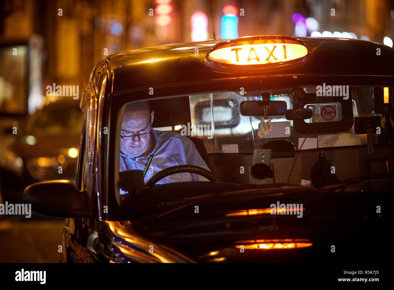 Liverpool city centre a late shift taxi driver resting using his mobile phone waiting in the rank Stock Photo