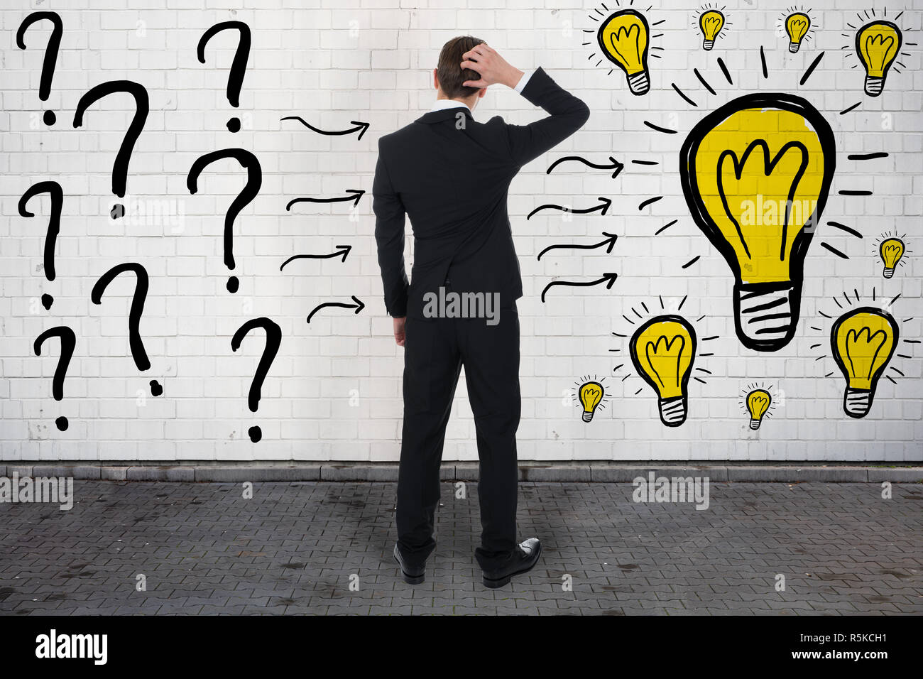Confused Businessman Looking At Question Marks And Light Bulbs Stock Photo