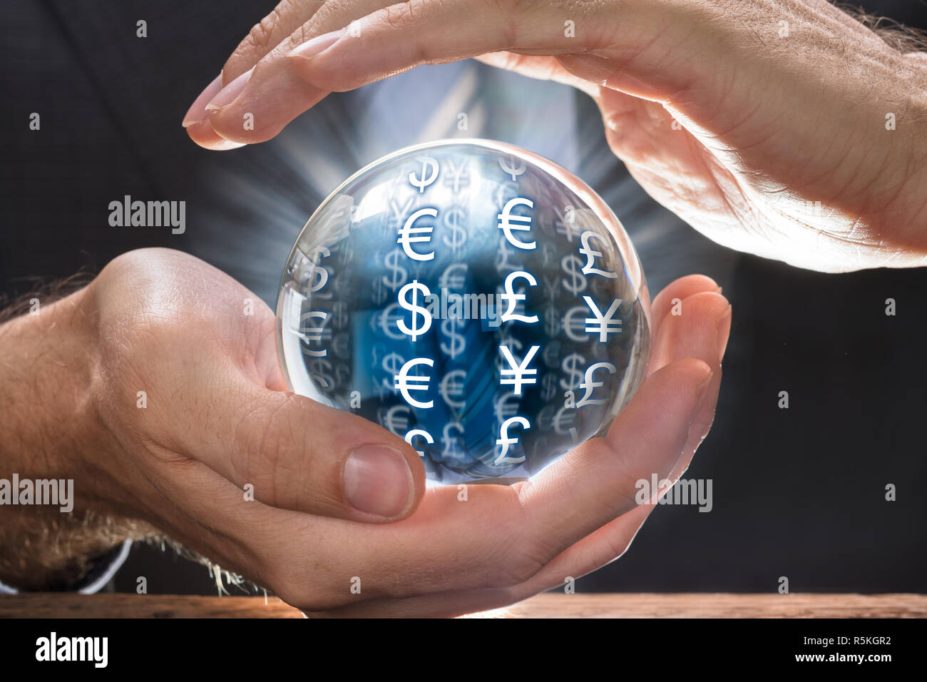 Businessman Covering Crystal Ball With Various Currency Symbols Stock Photo