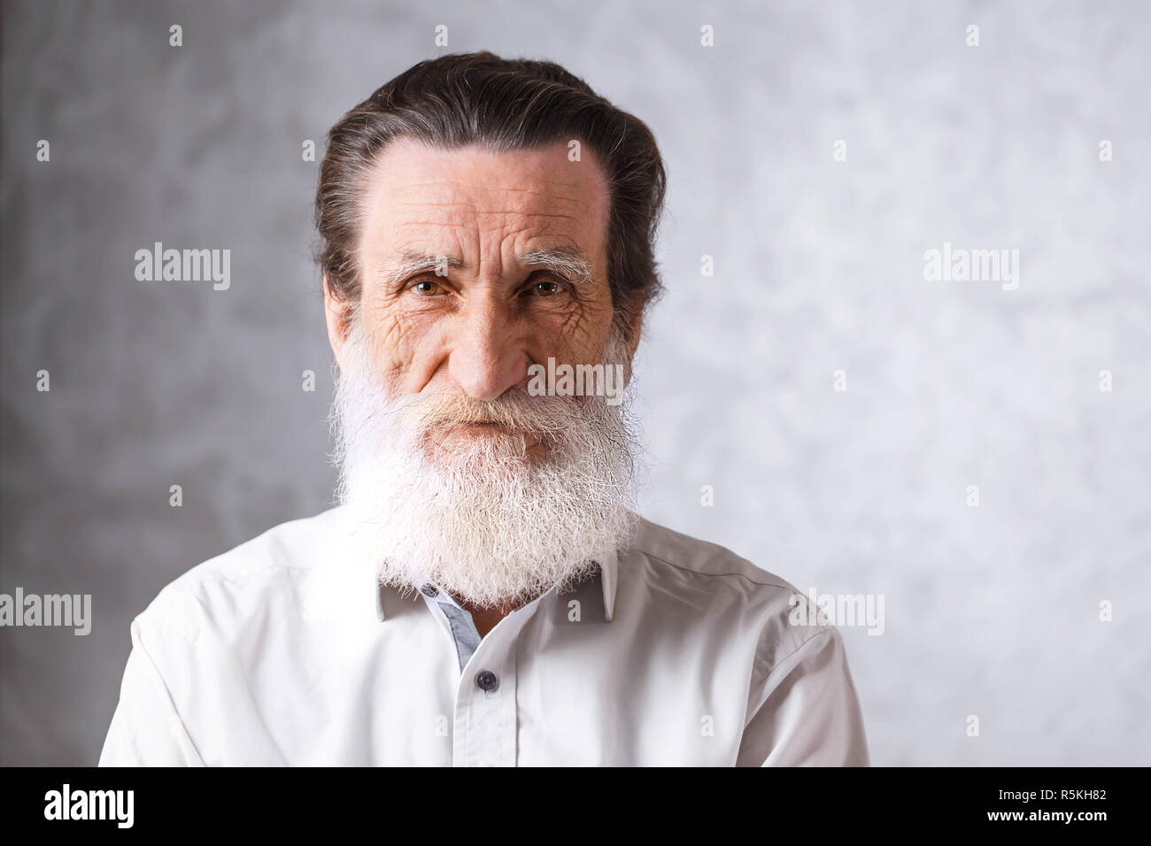 Portrait of contemporary senior bearded man with wrinkles in white shirt standing on the gray background, modern technology, communication concept Stock Photo