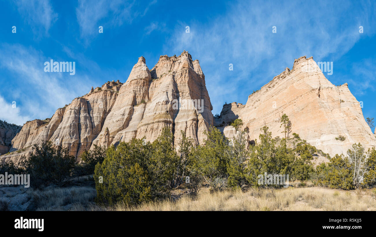Panorama of steep, sharp peaks and rock formations over a grassy meadow under a blue sky with wispy clouds at Kasha-Katuwe Tent Rocks National Monumen Stock Photo
