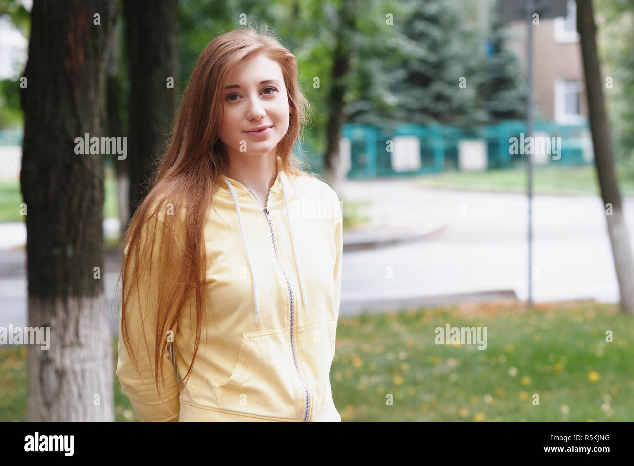 A pretty girl with long red hair, walks through the park and smiles ...