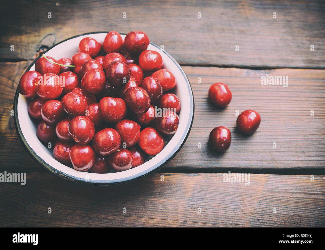 Ripe red cherry in an iron plate on a brown table Stock Photo - Alamy