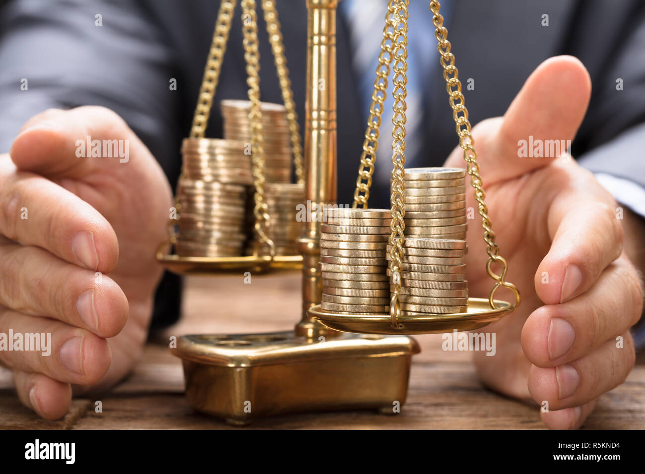 Businessman Covering Stacked Coins On Weighing Scale Stock Photo