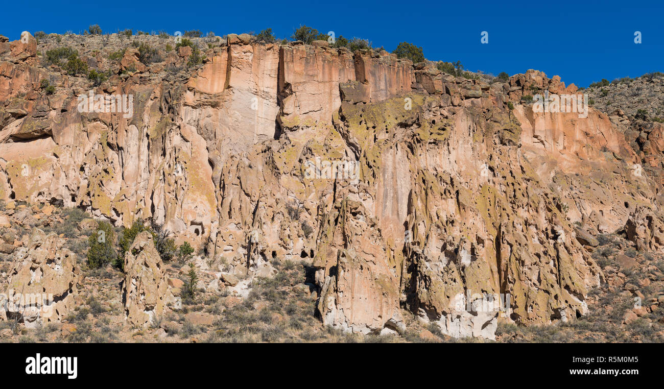 Panorama of highly textured, colorful high cliffs, caves, and ancient native American ruins an cliff dwellings in Bandelier National Monument near San Stock Photo