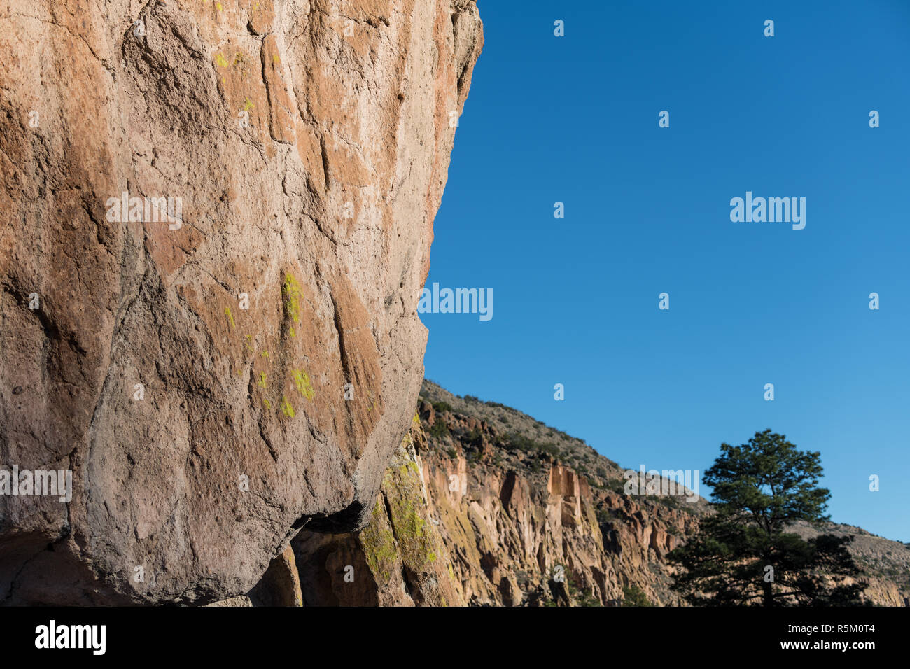 Overhanging colorful cliff of sandstone with yellow-green lichen in Bandelier National Monument Stock Photo