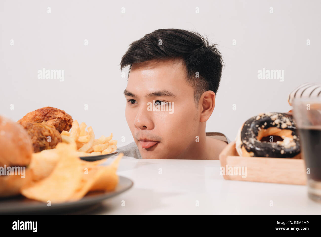 Young man having cravings for donuts, hamburger, chicken with fries instead Stock Photo