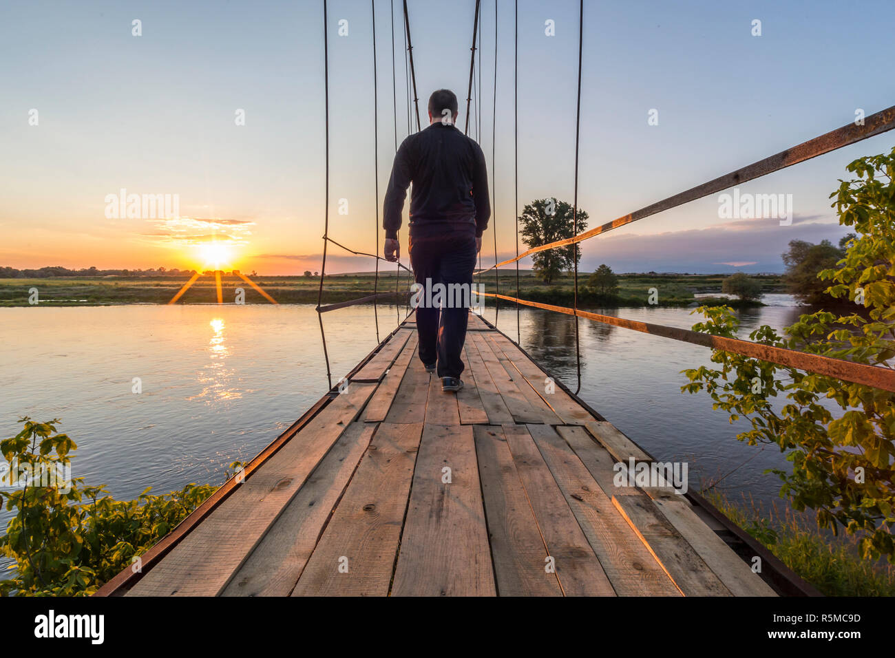 Man walking on an old suspension bridge towards the sunset Stock Photo ...