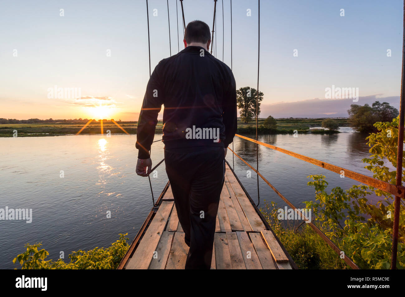 Man walking on an old suspension bridge towards the sunset Stock Photo ...