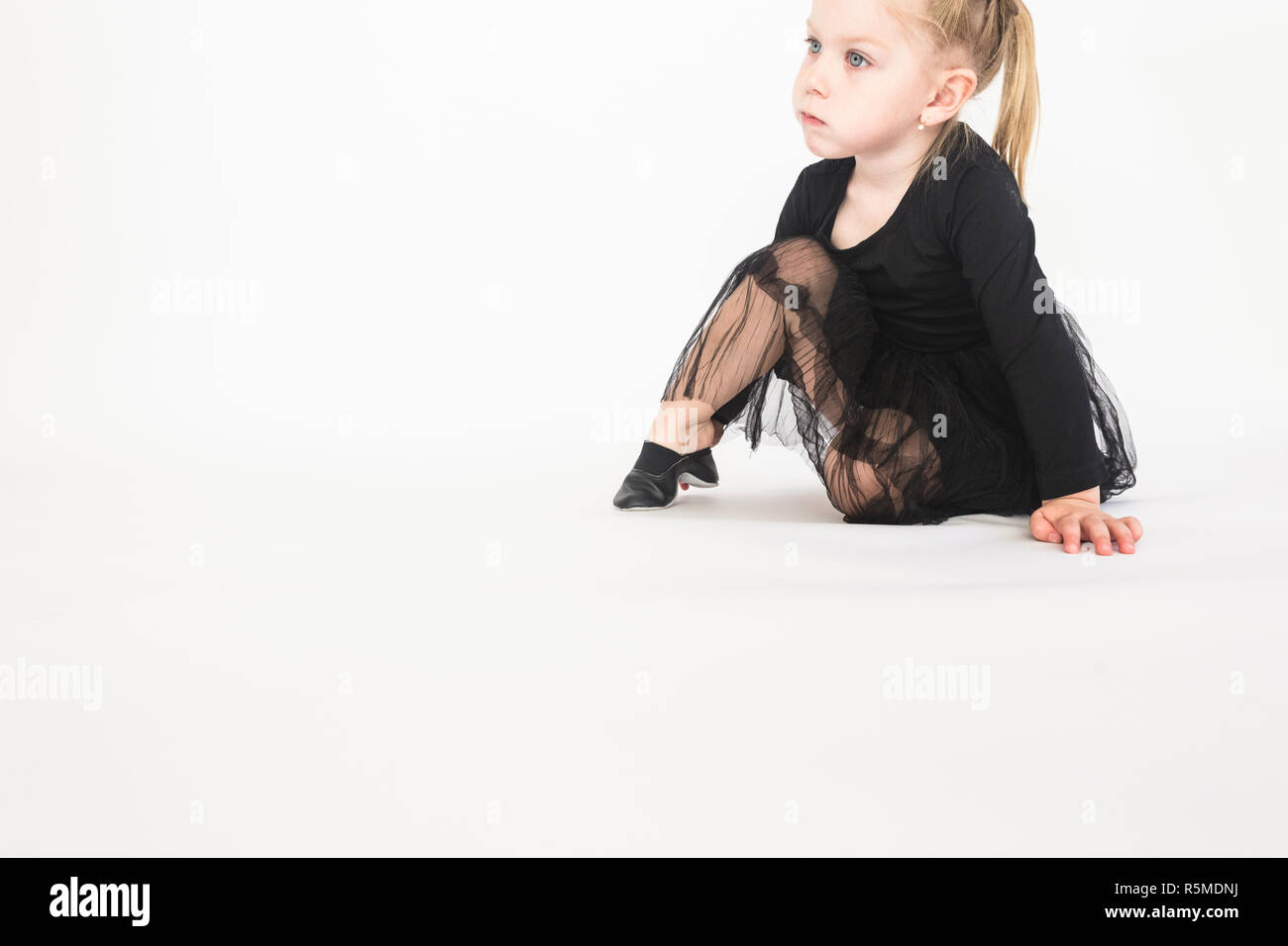 Cute little girl in beautiful black dress sitting on the floor on white ...