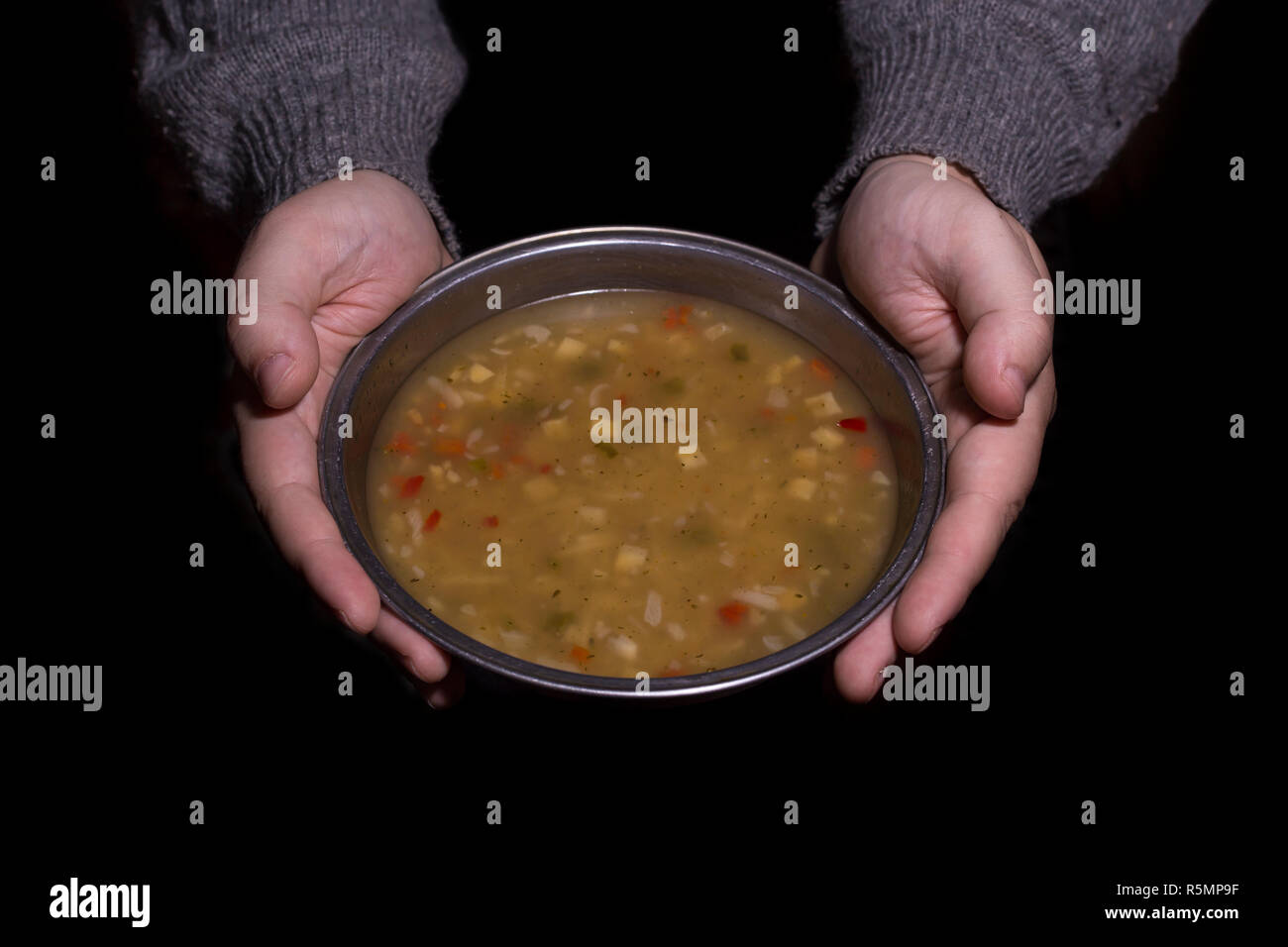 Poverty concept. Man holding a metal bowl of soup isolated on black background. Stock Photo