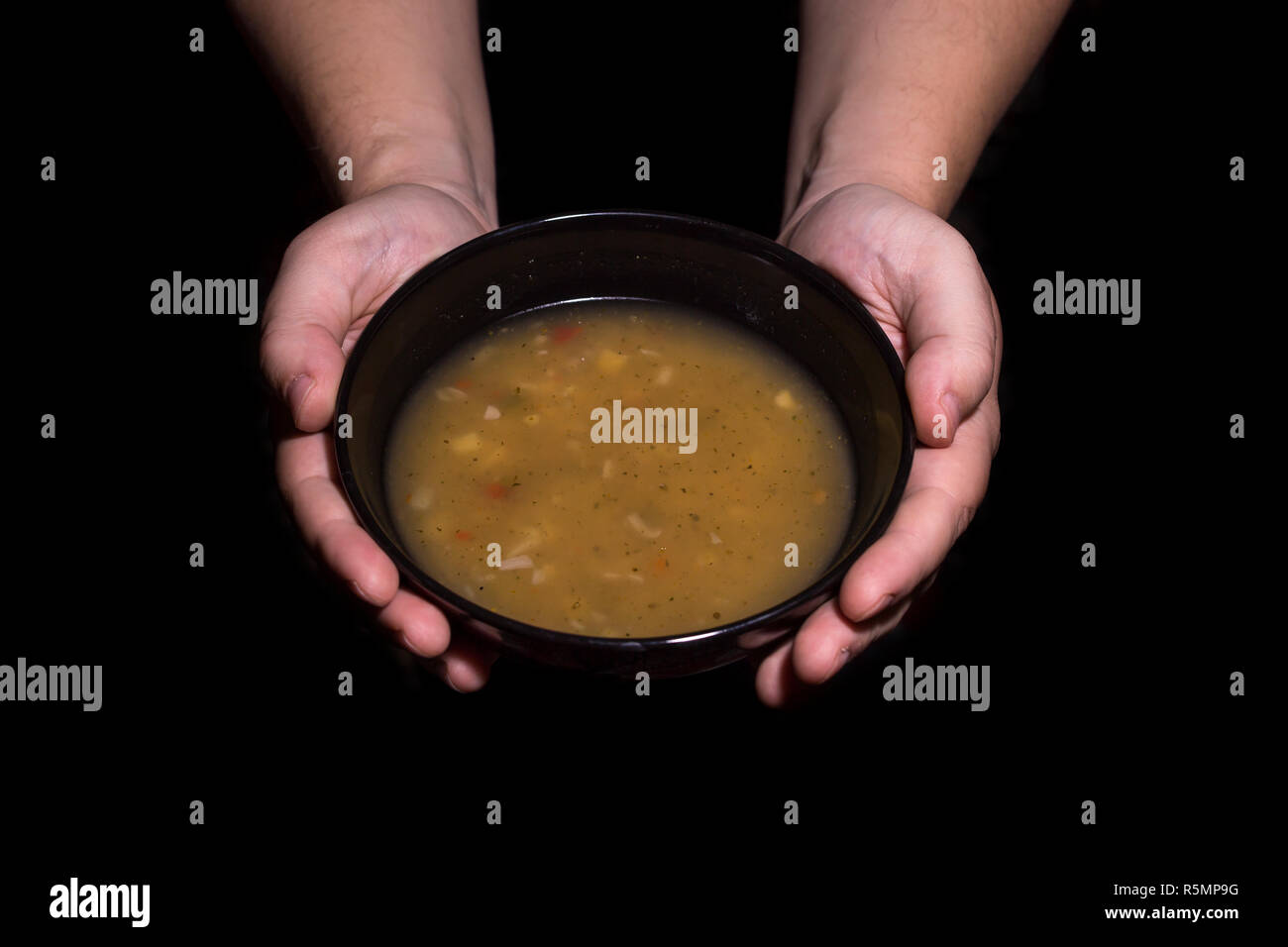 Poverty concept. Man holding a bowl of soup isolated on black background. Stock Photo