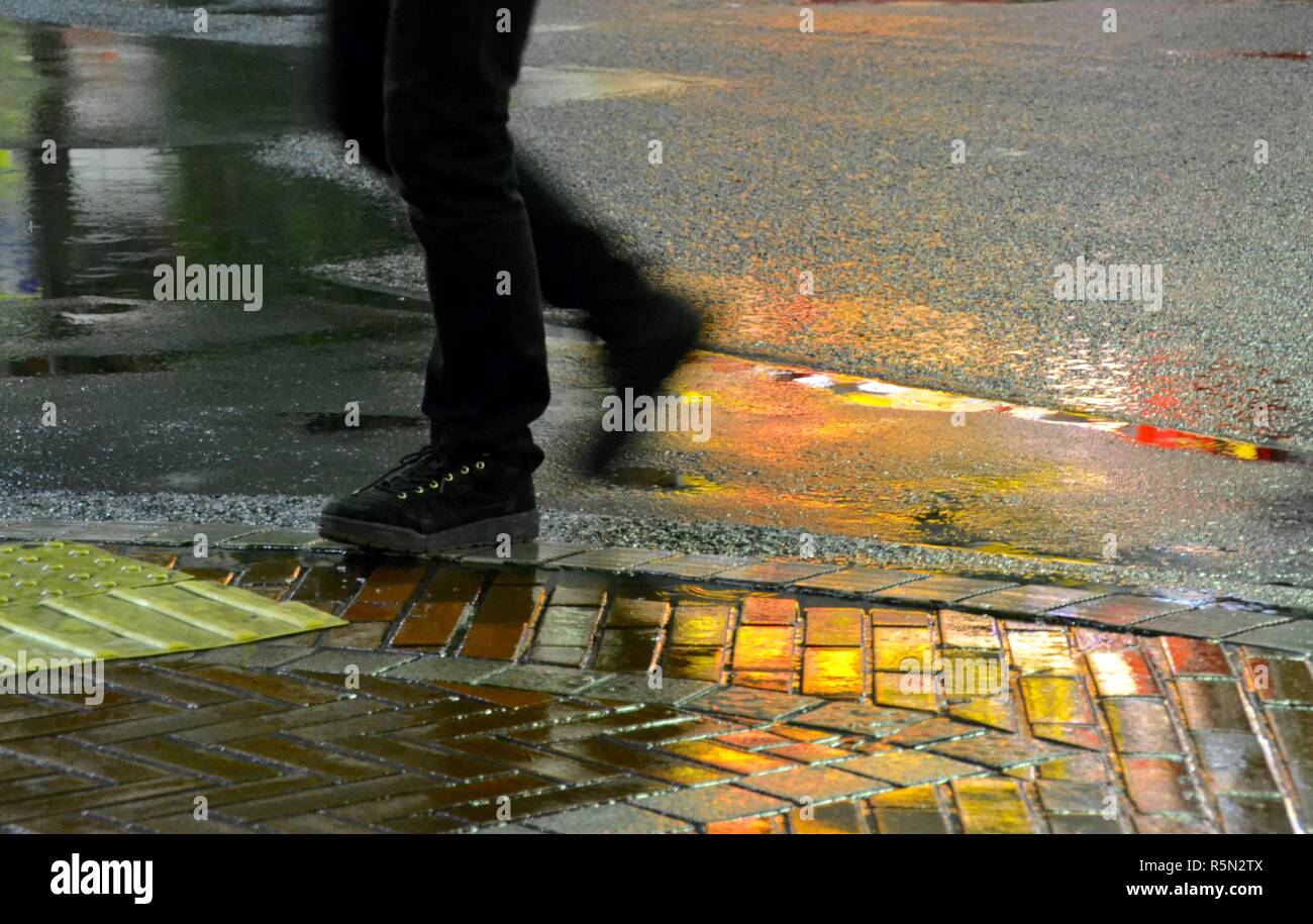 Black jeans and sneakers splashing through the puddles on a wet rainy Tokyo night with neon light reflected on the paving stones and road Stock Photo