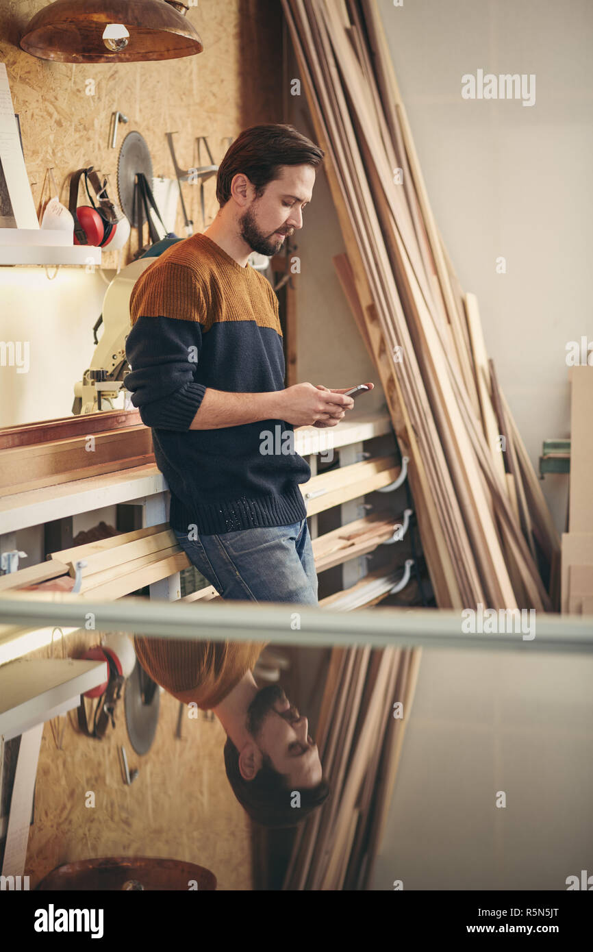 Young craftsman using phone in his workshop Stock Photo