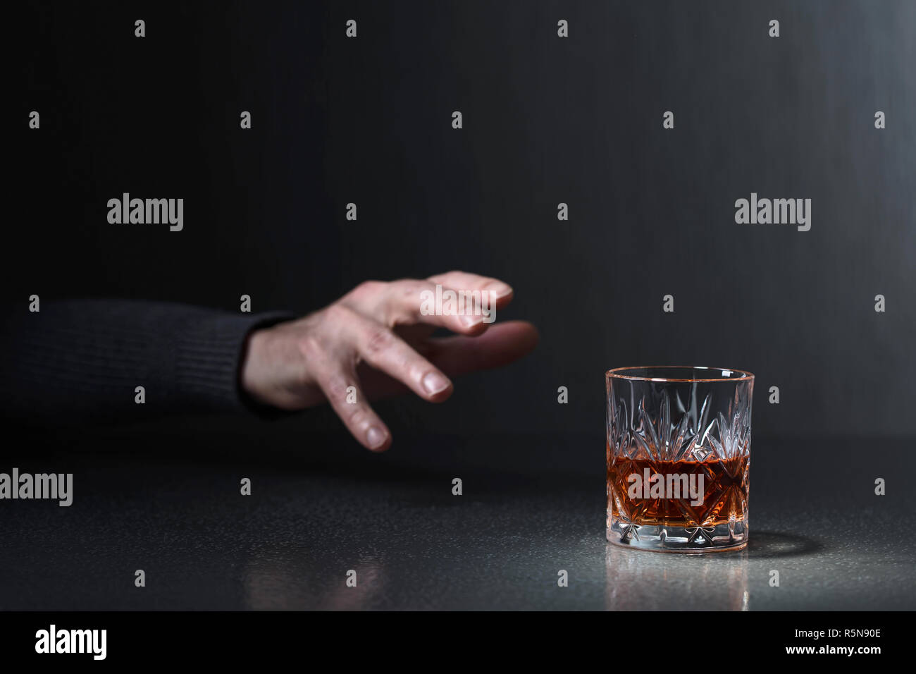 Man's hand reaches for a glass of alcohol. Conceptual image on the