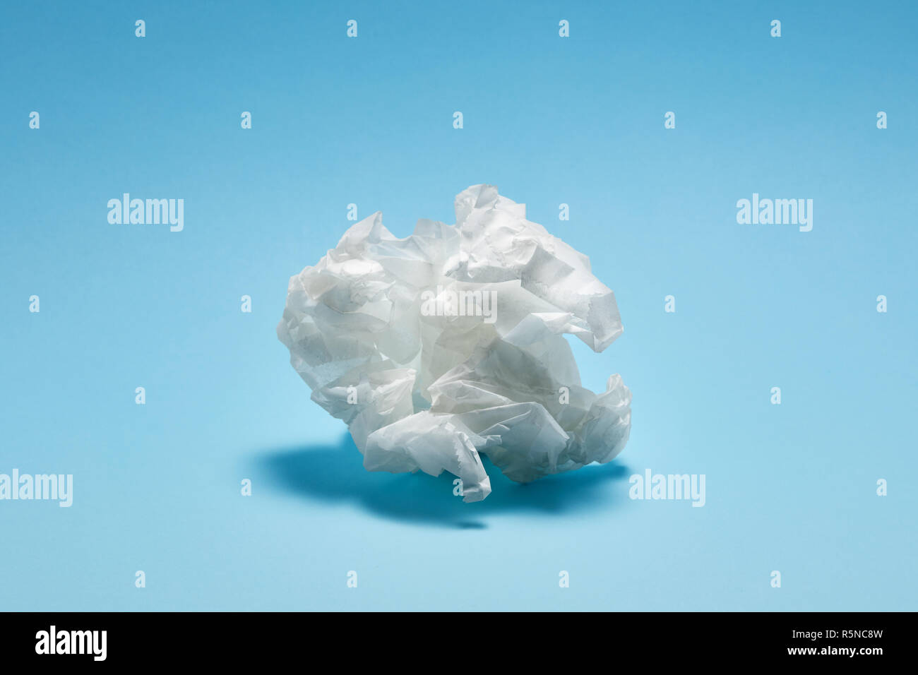 Crumpled white paper texture on light blue background under dramatic moody lighting Stock Photo