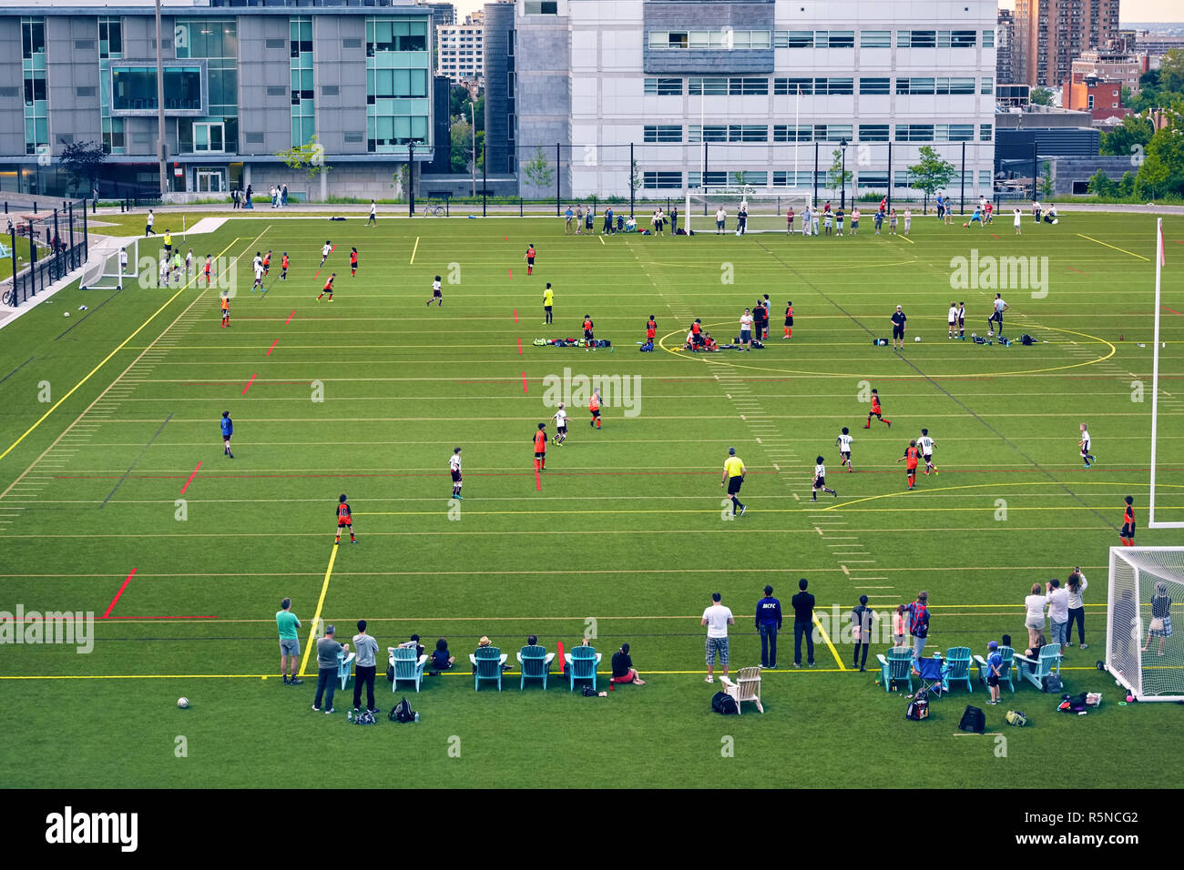 Kids are playing soccer on the football field and the parents are