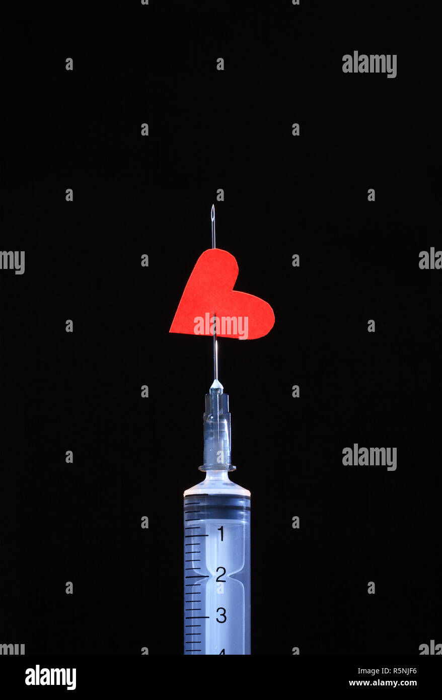 Plastic syringe with red paper heart on the needle isolated on black background Stock Photo