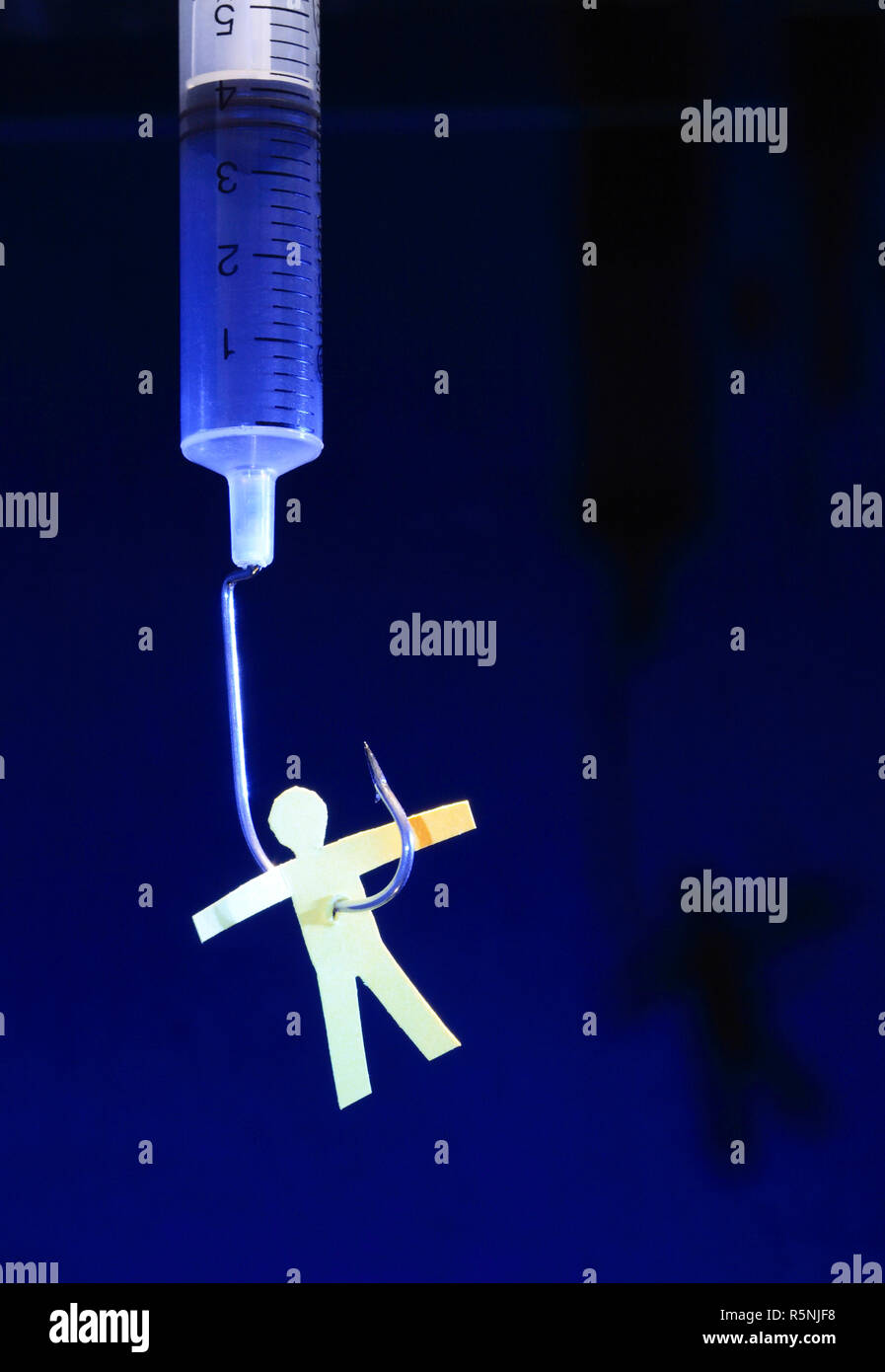 Yellow paper man hanging on syringe with fish hook on dark background Stock Photo
