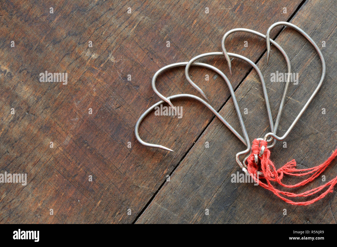Five fishing hooks lying on dark wooden background Stock Photo