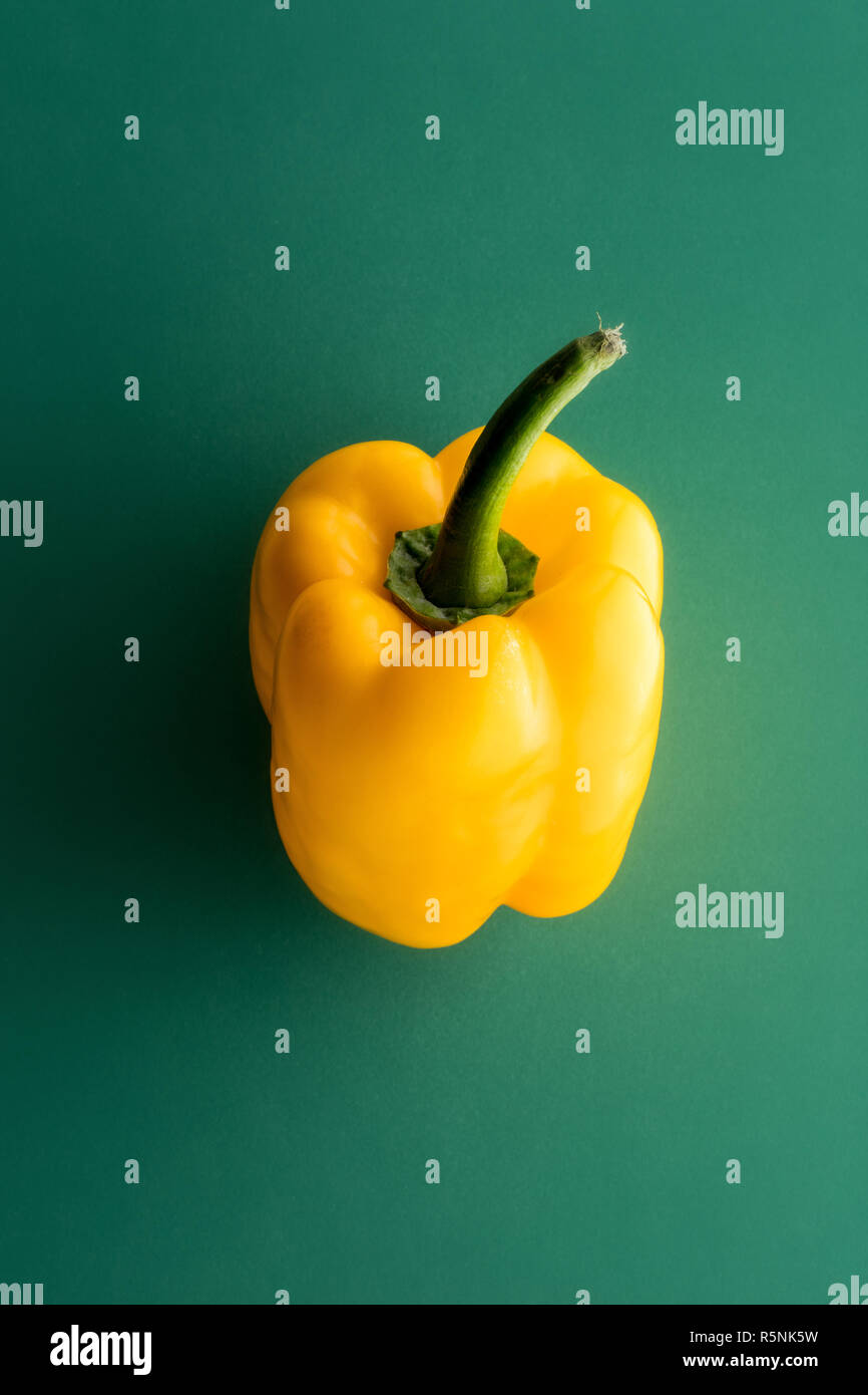 One whole yellow sweet pepper on green background, viewed from above in close-up Stock Photo