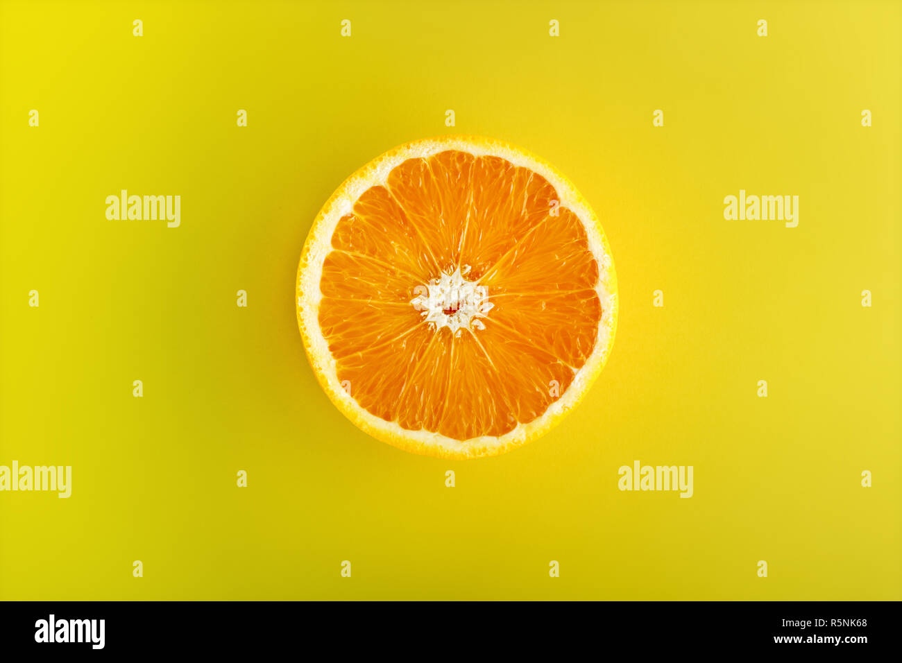One half of sliced ripe orange viewed from above in center isolated on yellow background Stock Photo