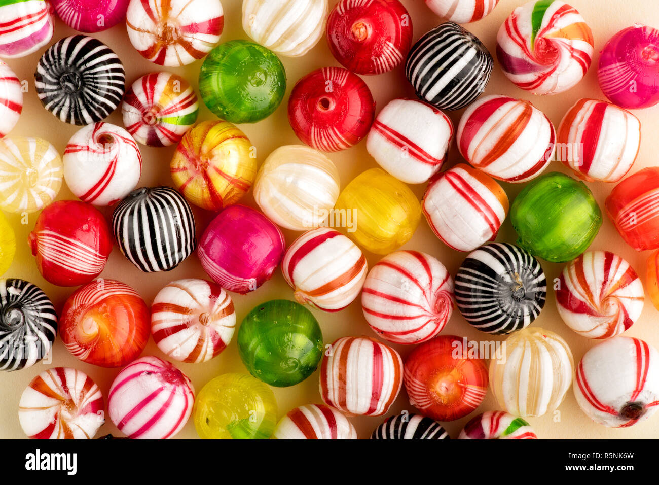 Colorful round candies of red, white, green, yellow and black colors with stripes, sitting on table surface in one layer, top view in full frame Stock Photo