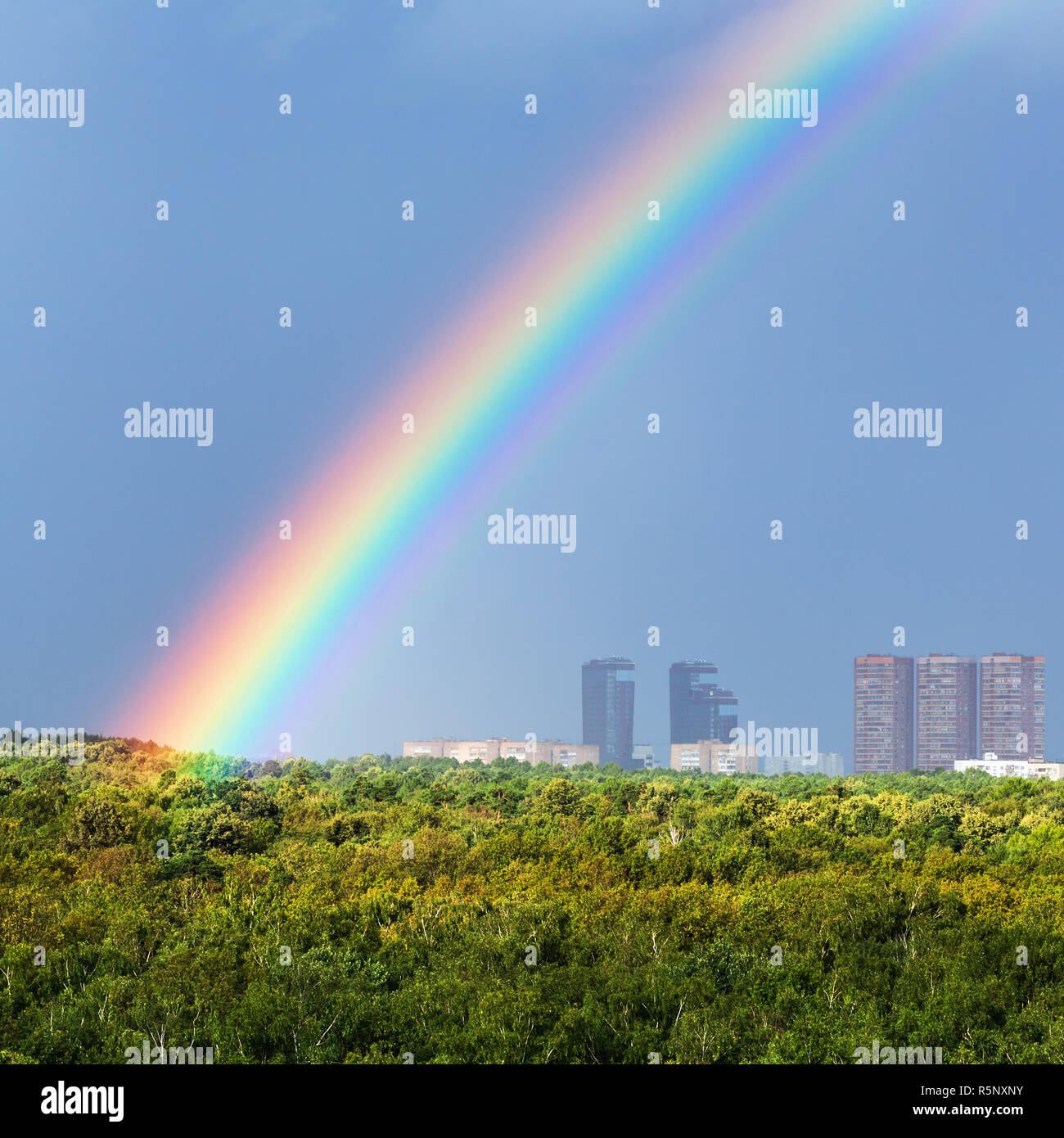 rainbow in blue sky over city and green trees Stock Photo - Alamy