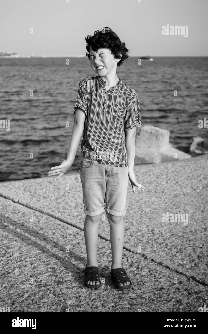A disgruntled boy is standing by the sea. Black and white. Stock Photo
