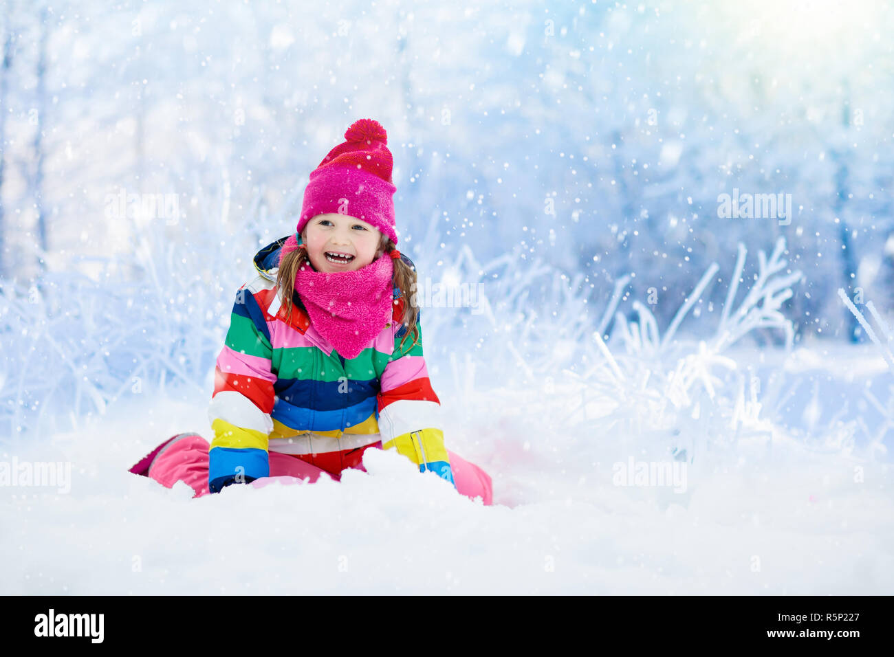 Child playing with snow in winter. Little girl in colorful jacket and ...