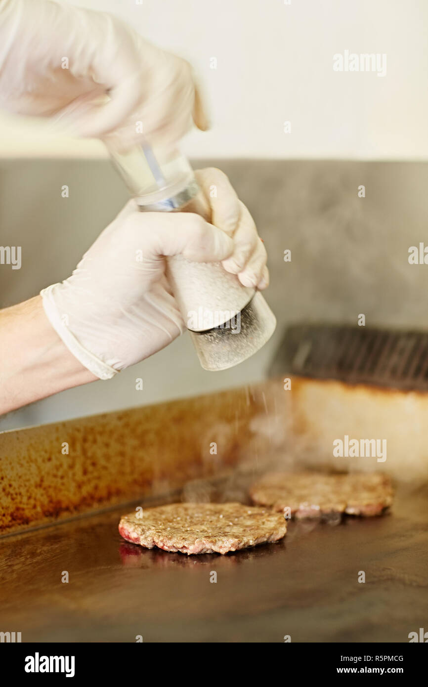 Chef's hands grinding salt to season frying hamburger patties Stock