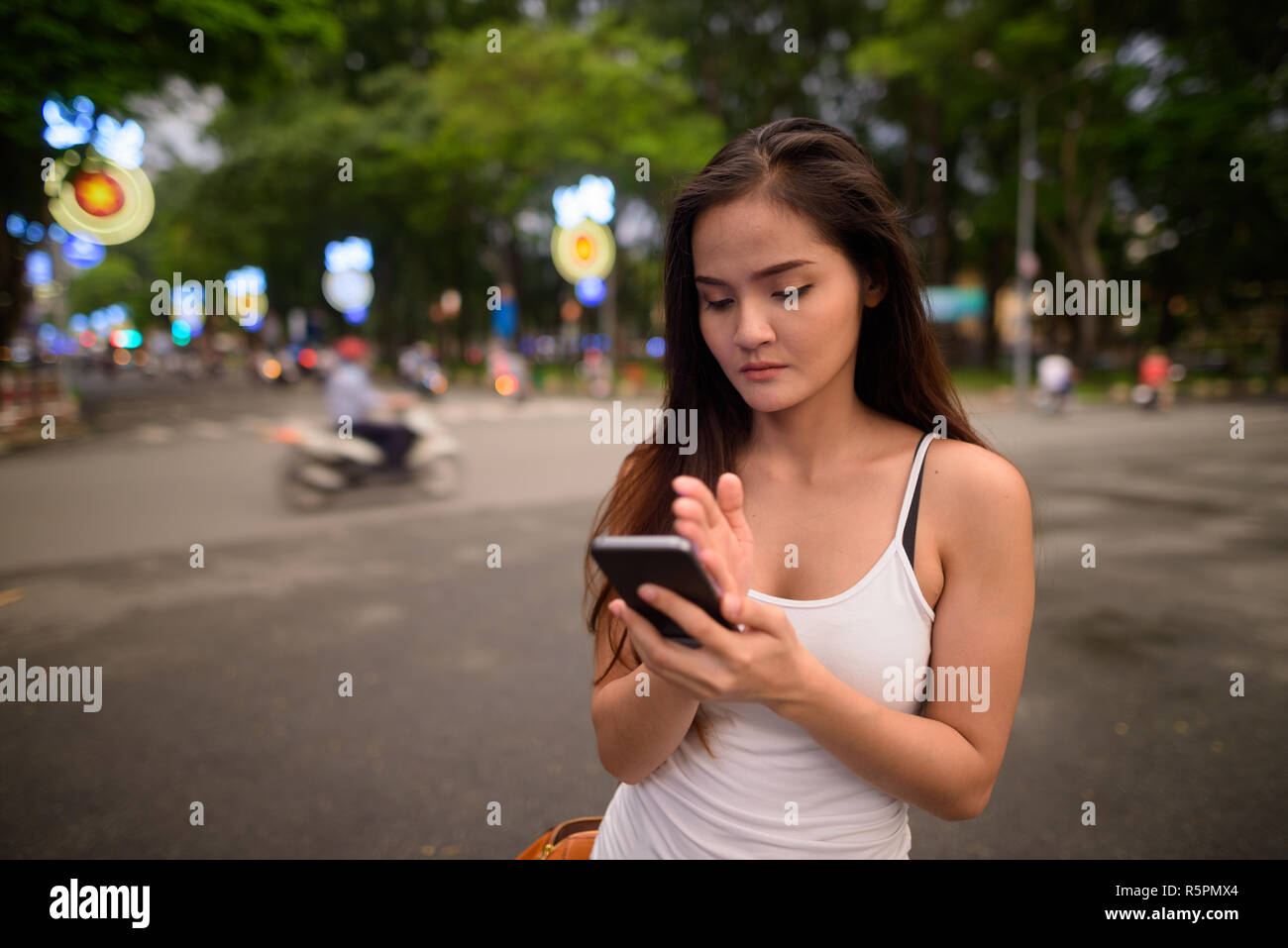 Young beautiful Asian tourist woman using mobile phone outdoors Stock Photo