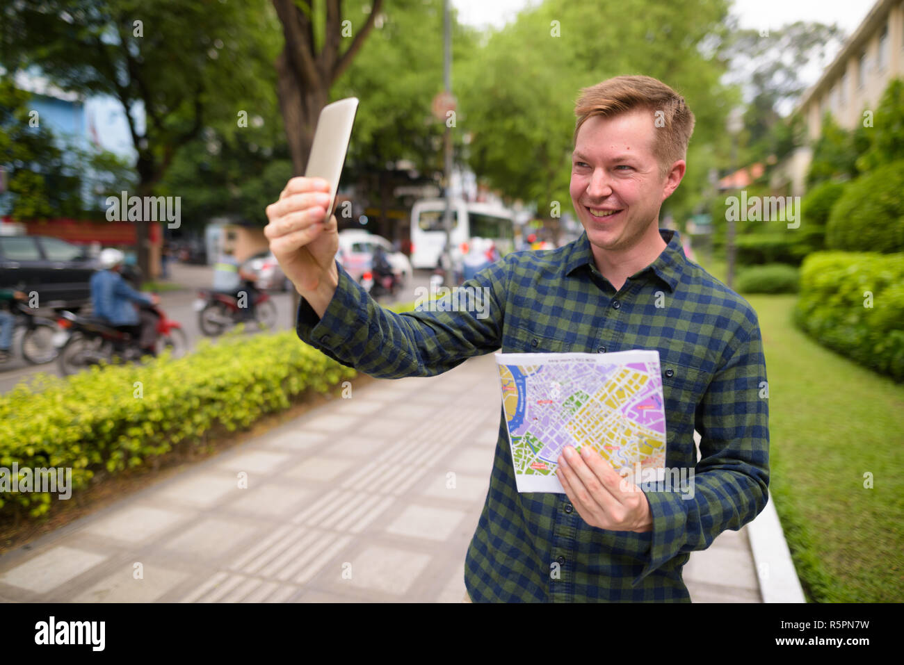 Tourist man holding map and taking selfie with mobile phone Stock Photo