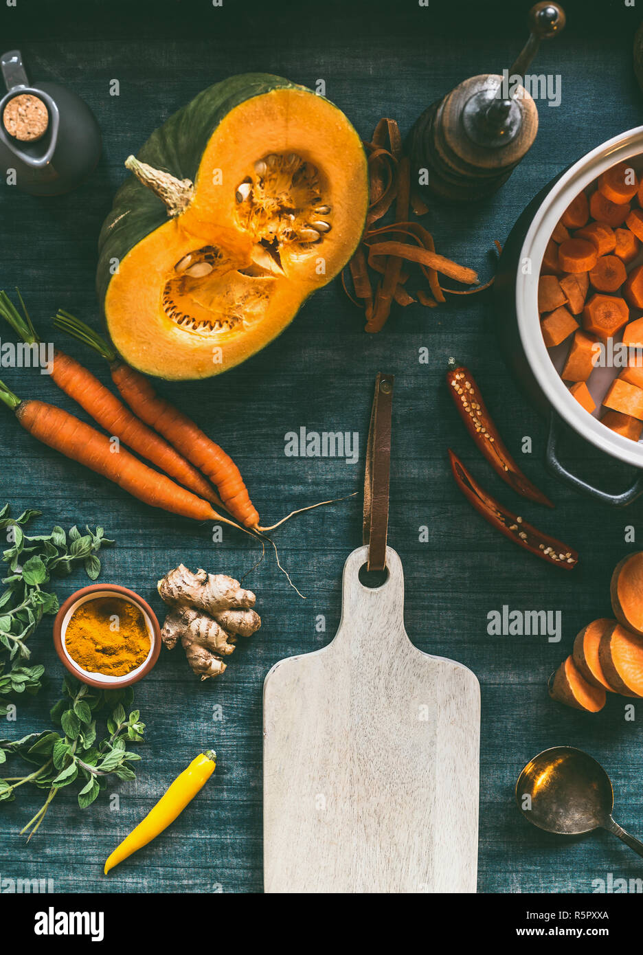 Orange color cooking ingredients around cutting board. Pumpkin, carrots,sweet potatoes, turmeric, chili and fresh seasoning for healthy vegetarian sou Stock Photo