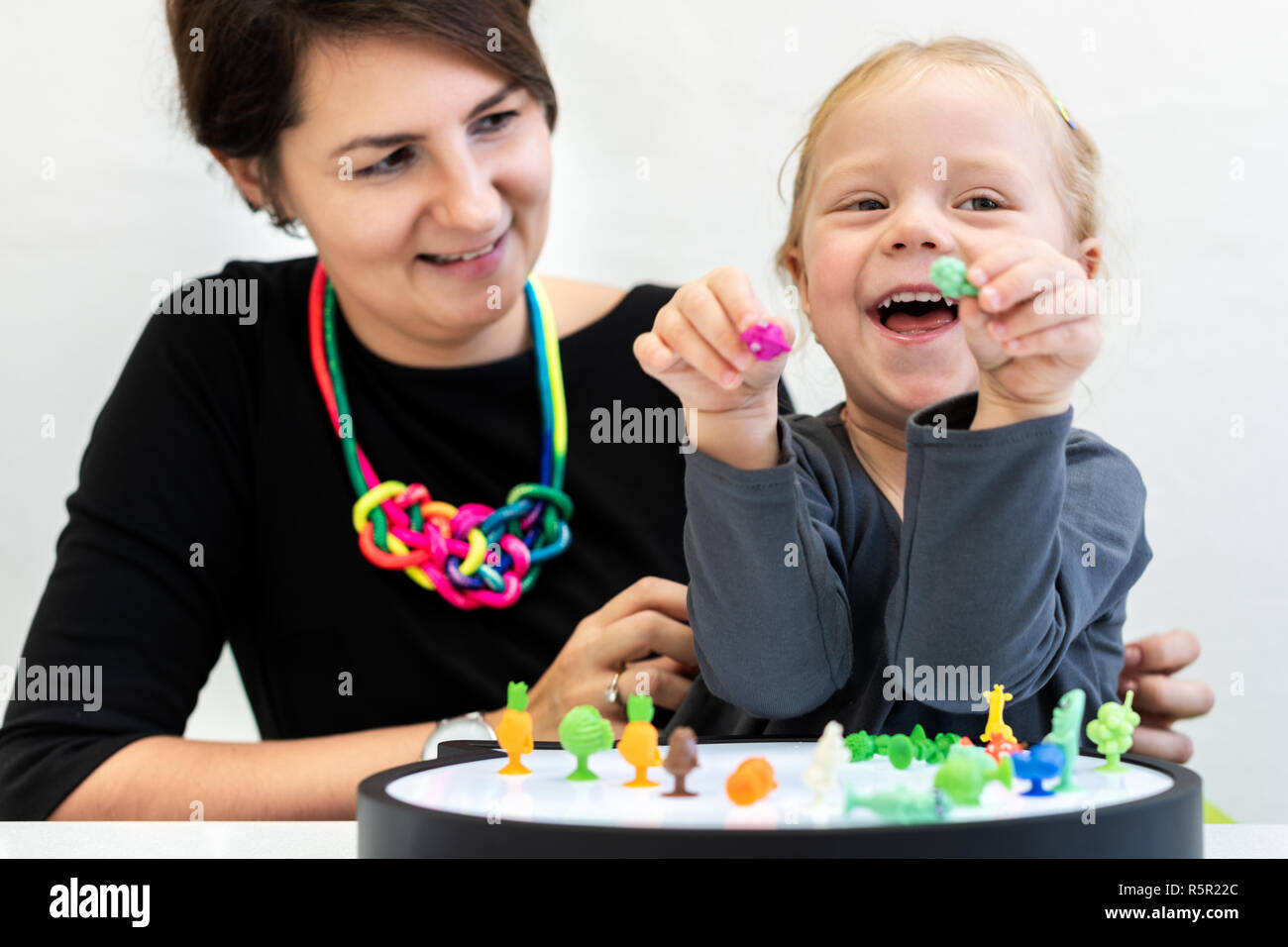Toddler girl in child occupational therapy session doing sensory playful exercises with her therapist. Stock Photo