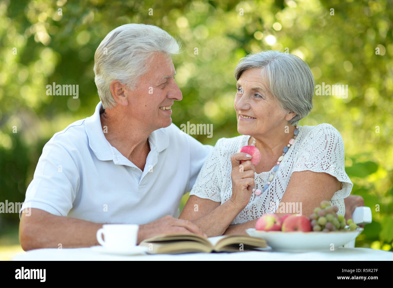 Portrait of beautiful old couple reading book at table in summer Stock Photo