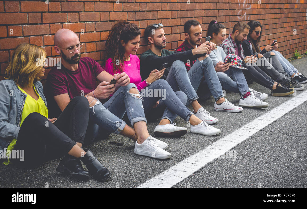 Eight millenials students smiling and looking at their cellphones. Concept of youth, tech, social and friendship Stock Photo