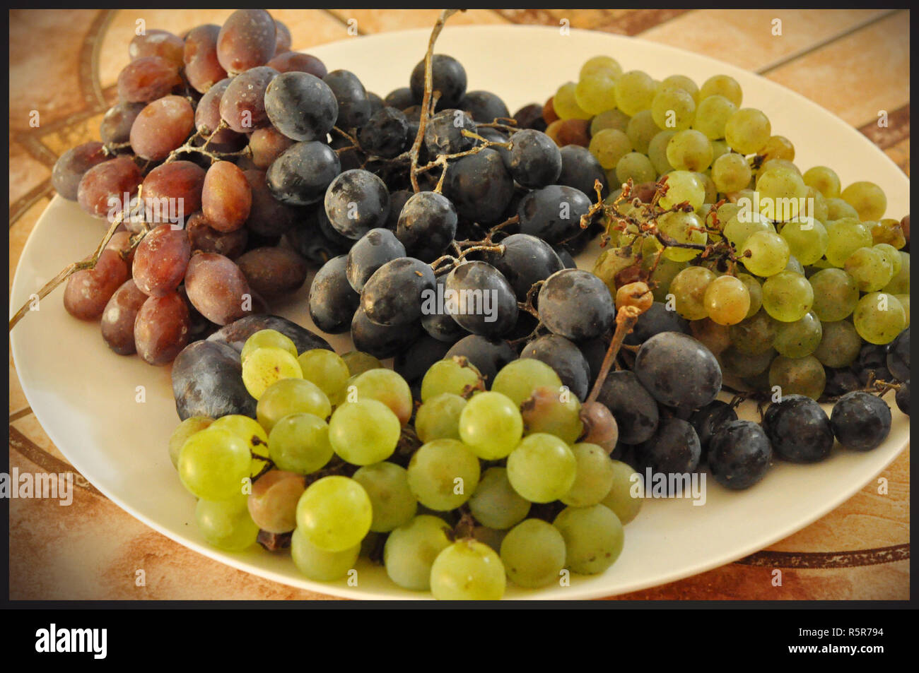 A white plate with different grape varieties - red and white, rounded and round and elongated table grapes Stock Photo