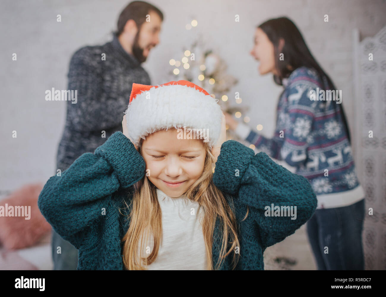 Sad, desperate little girl during parents quarrel. Clog the ears.. Family quarrel on the eve of Christmas. Stock Photo