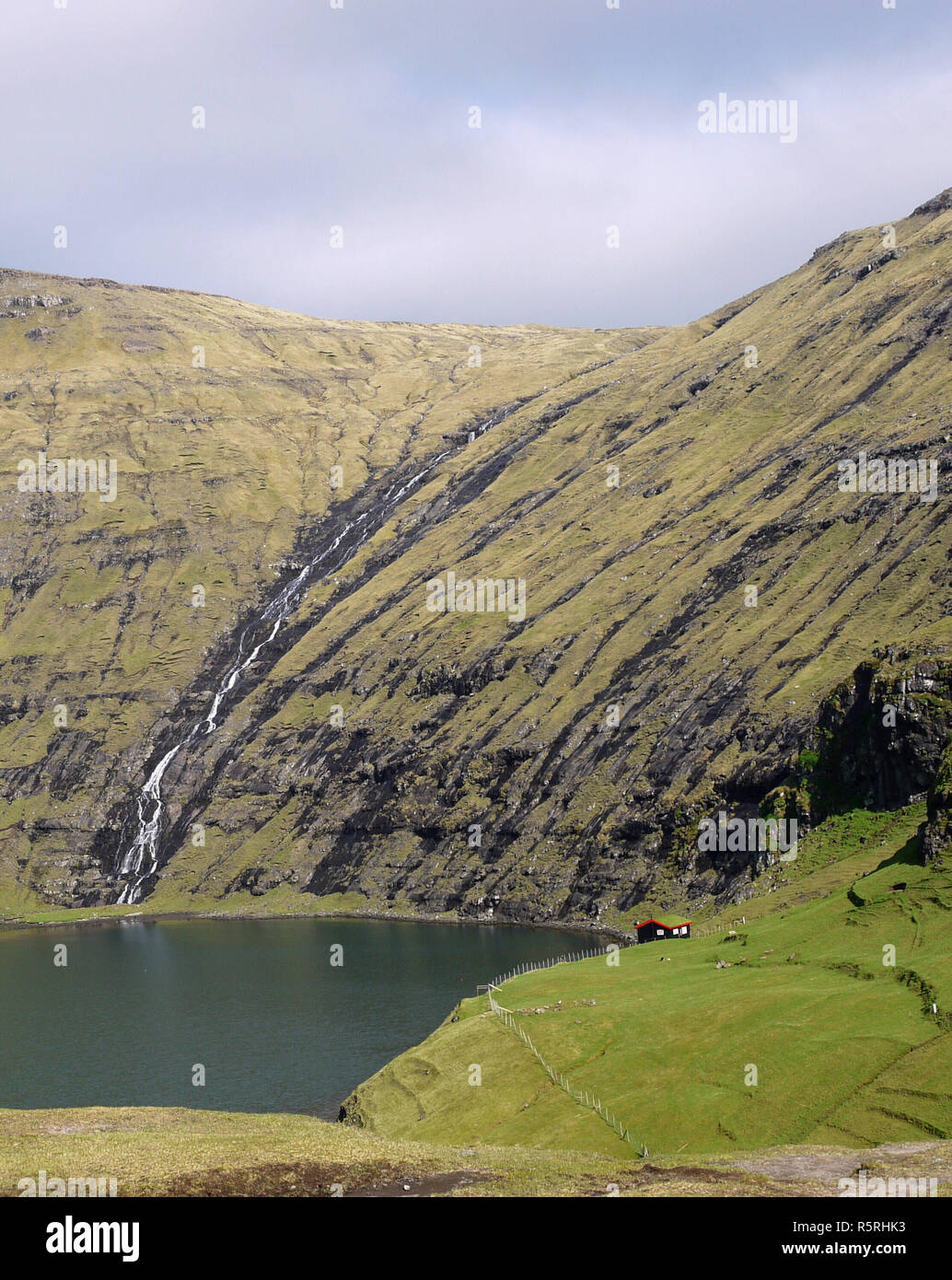 Waterfall at Saksun with tiny red tin roof house on the side of the sea inlet in the Faroe Islands Stock Photo