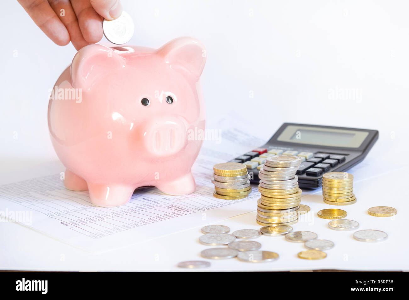 Hand inserting coin into piggybank Stock Photo